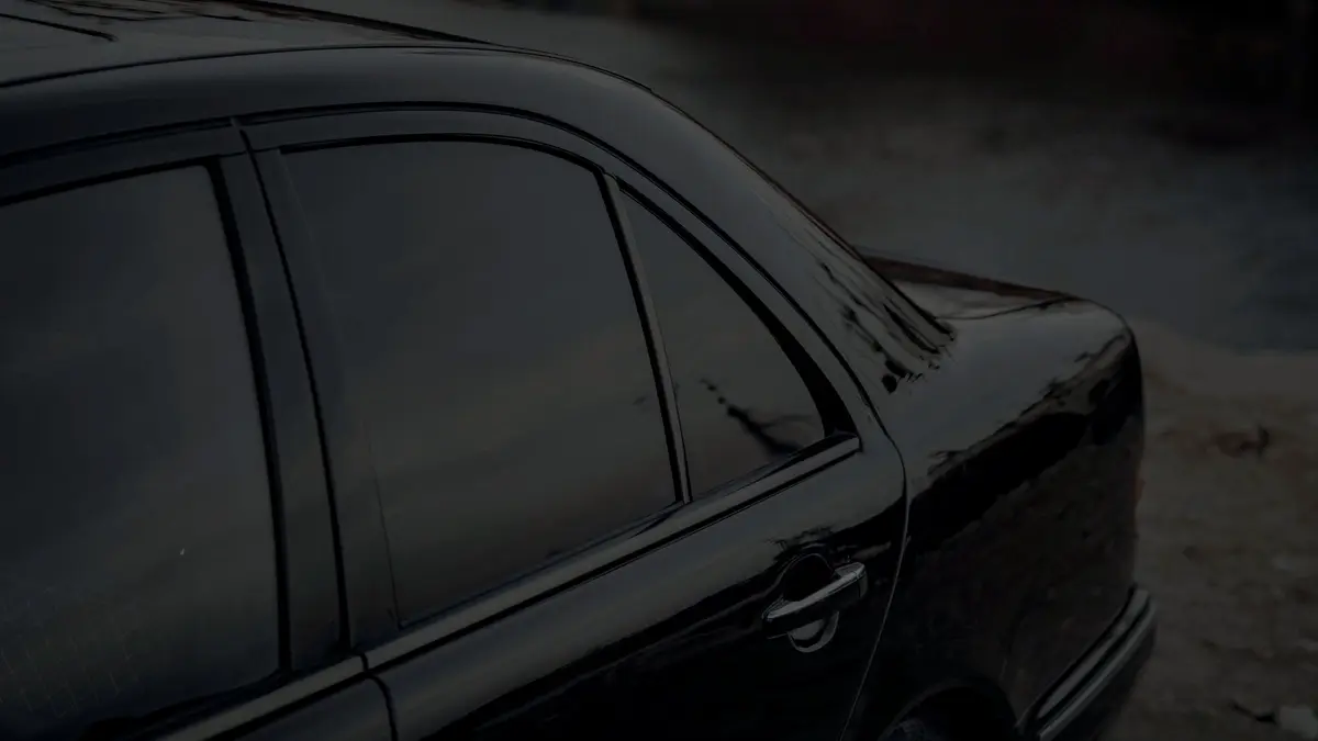 Koyu renkli bir sedanın karartılmış yan camları, loş ışıkta yakın plan